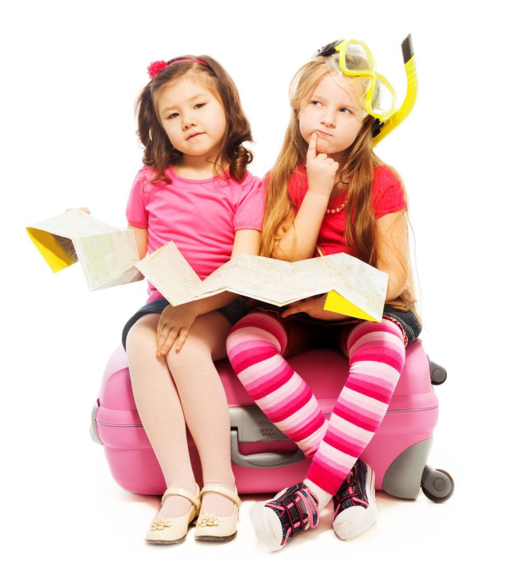 Two cute little exited girls sitting on suitcase with map preparing to travel deciding destinations, wearing snorkel and mask, isolated on white